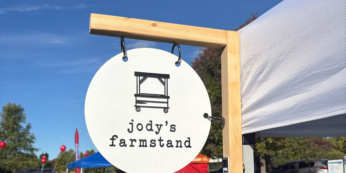 Round hanging Jody's Farmstand sign against a blue sky